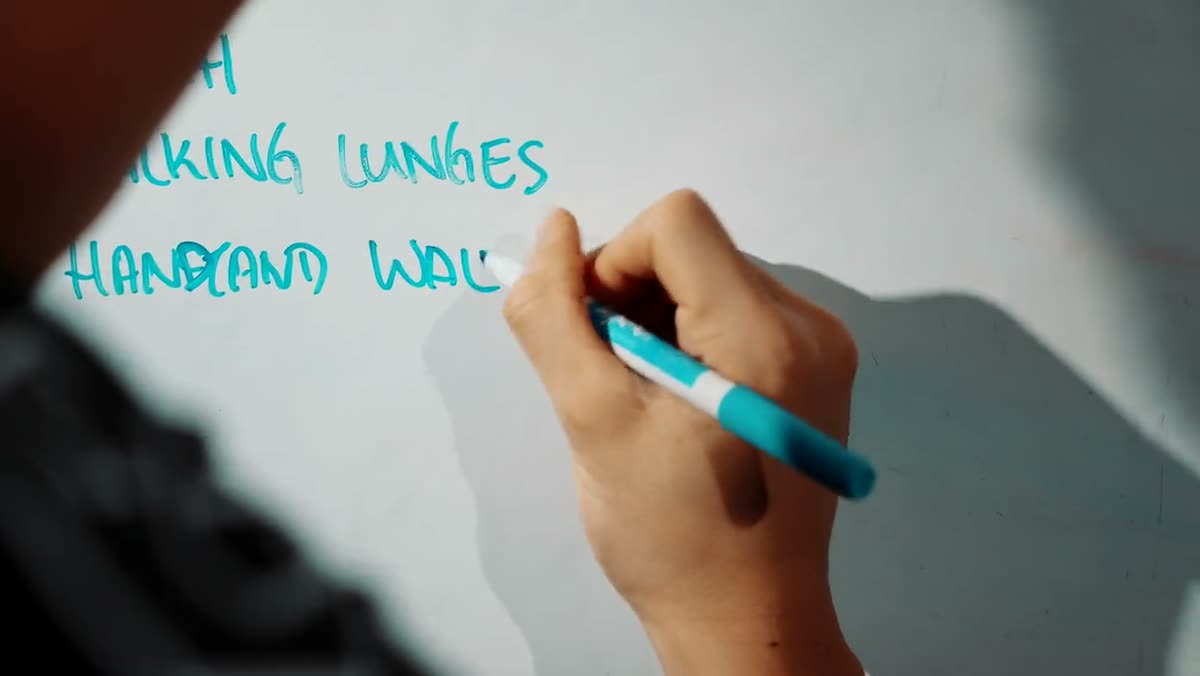 A hand writing the day's workout on a whiteboard in teal marker.