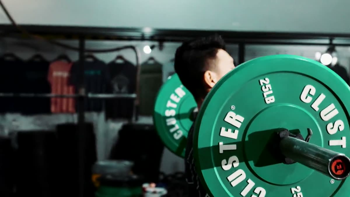A member loading green bumper plates onto a barbell.