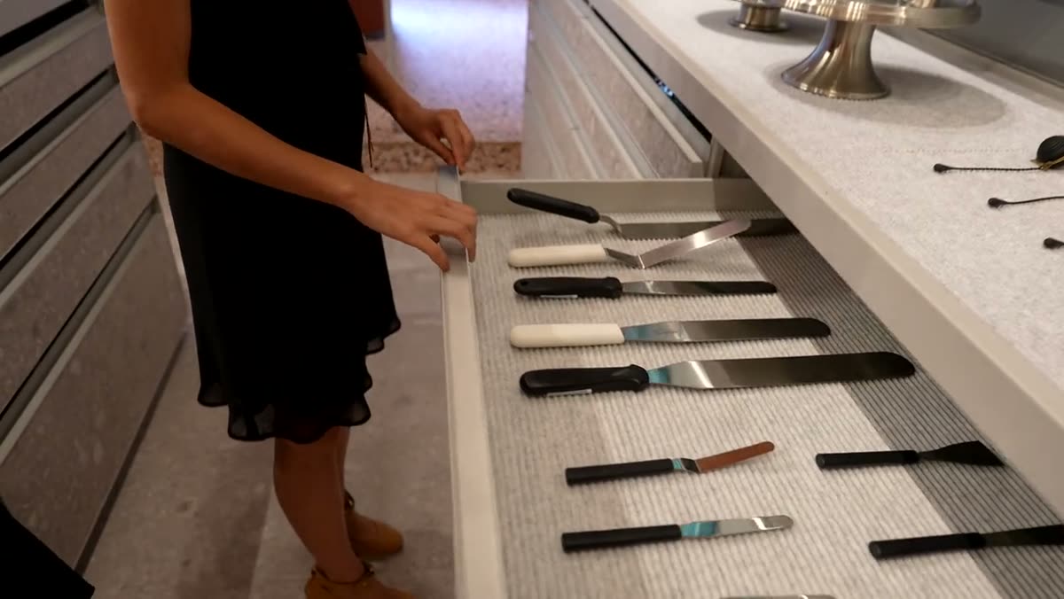 A hand selecting from a row of palette knives on a display counter.