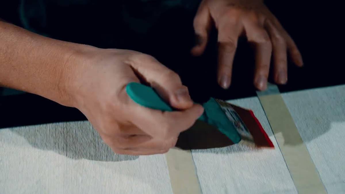 A hand pressing masking tape down onto a panel.
