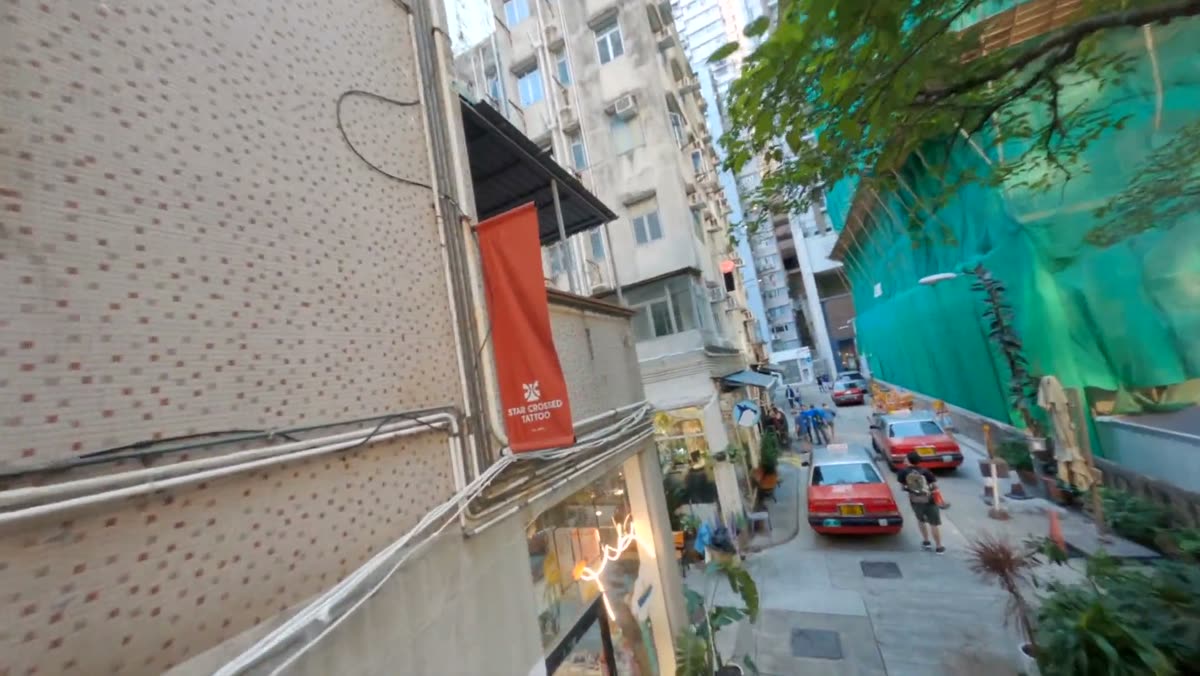 An FPV drone flying down a Hong Kong side street toward the studio banner.