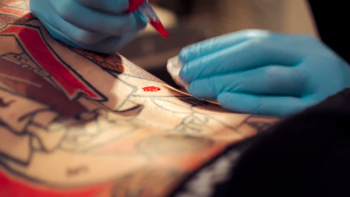Gloved hands working colour into a large back tattoo.