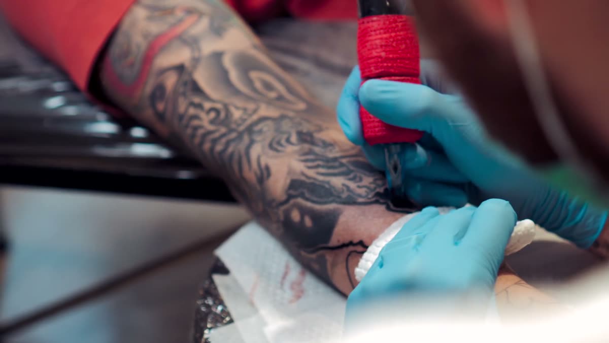 An artist wiping down a sleeve tattoo in progress.