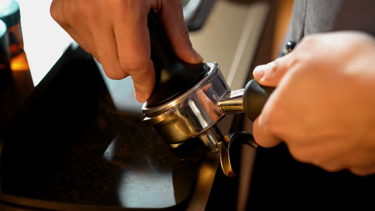 Hands tamping coffee into a portafilter.
