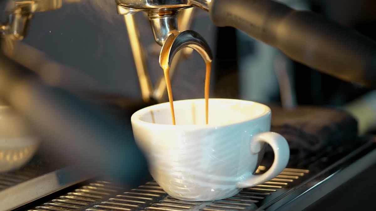 Espresso pouring from a group head into a white cup.