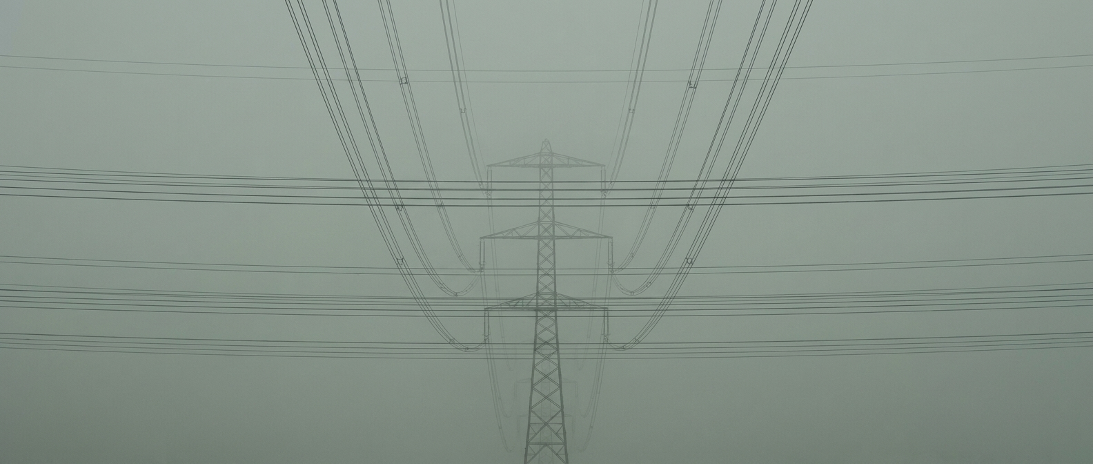 Transmission lines running to the horizon, compressed by a long lens into a stack of near-parallel horizontal bands that never converge.