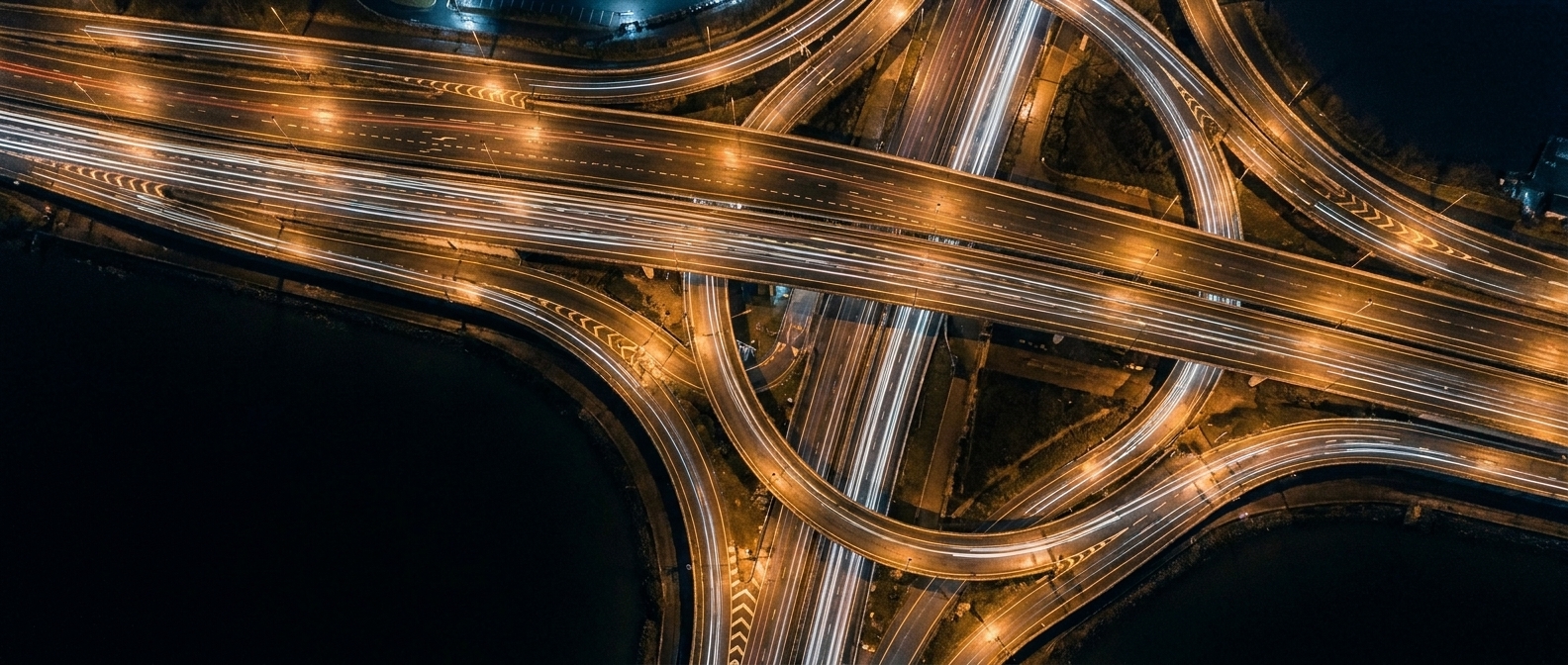 A motorway interchange from above at night, dense with light trails.
