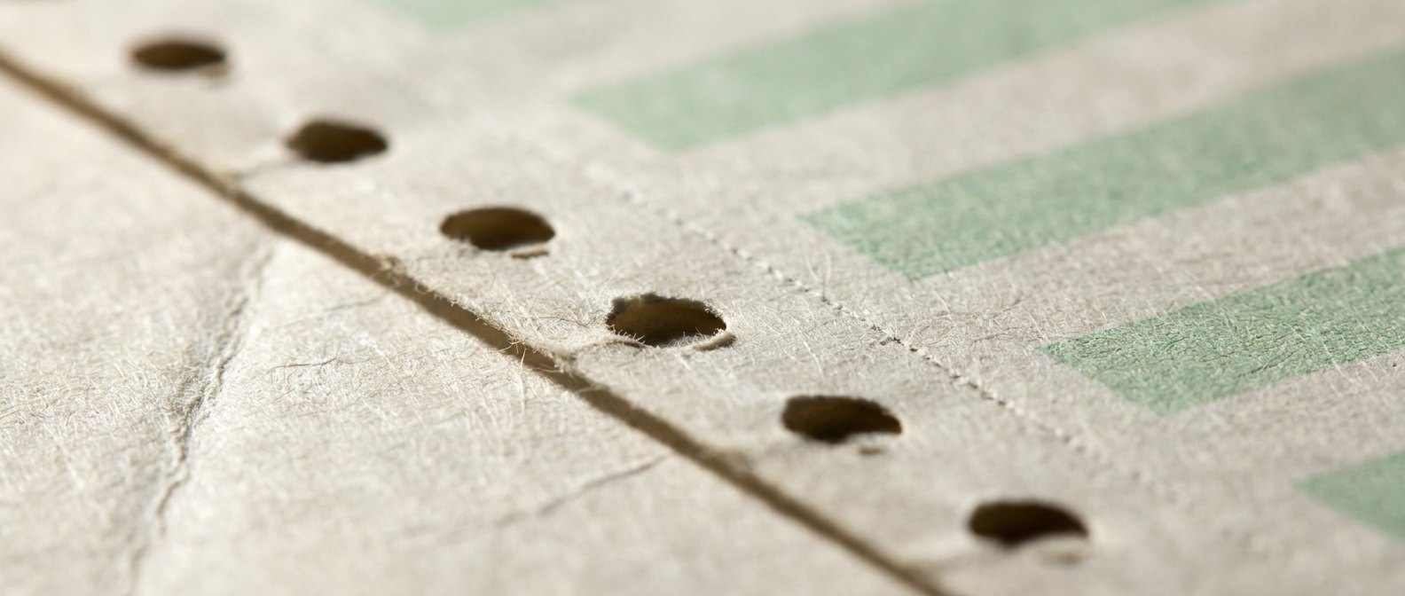 Extreme macro of green-bar continuous-form paper, the perforated tractor-feed margin running across the frame under raking light.